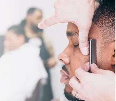 A barber shaping a man's beard with a straight razor.