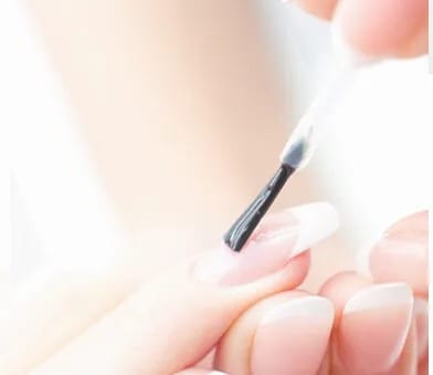 Close-up of applying clear nail polish on fingernails.