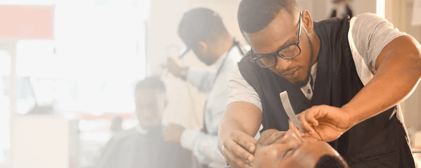 Barber giving a haircut to a smiling customer in a barbershop.
