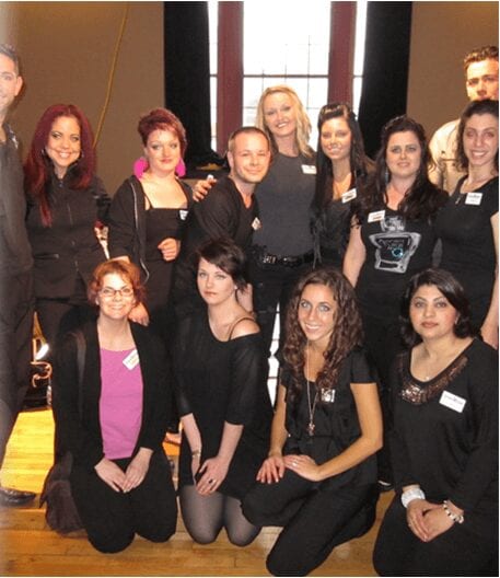 Thirteen adults from different ethnicities dressed in black posing together for a group photo 
